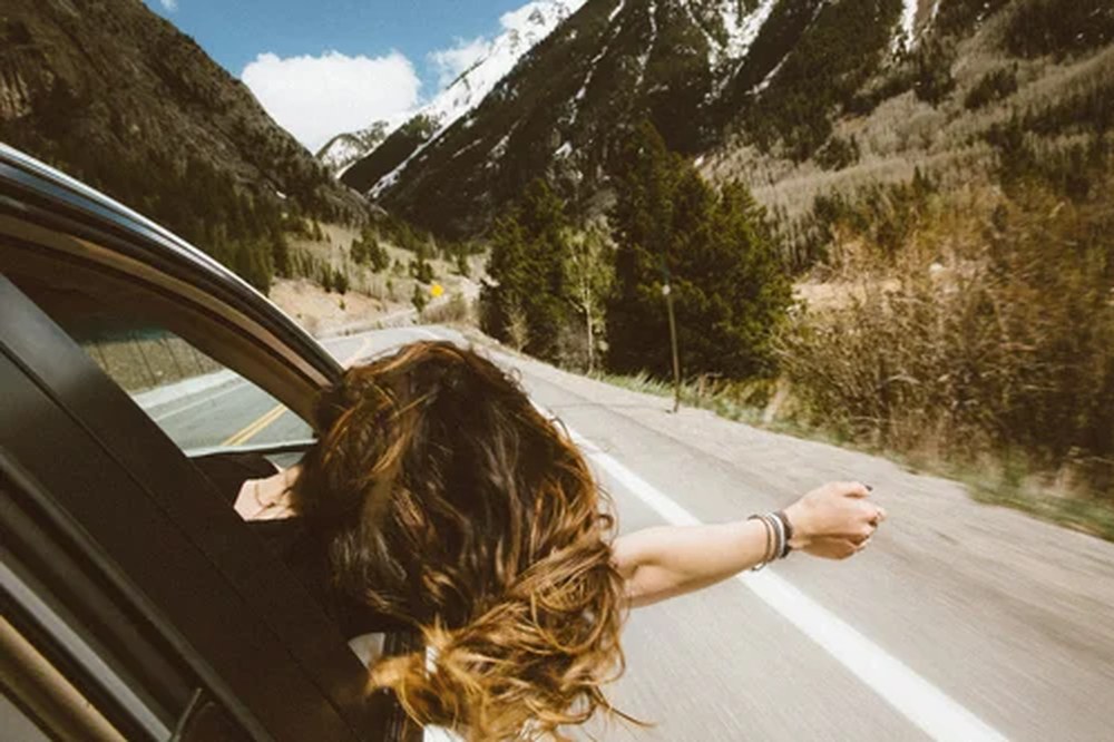 A woman with her hand out an open car window on an open mountain road